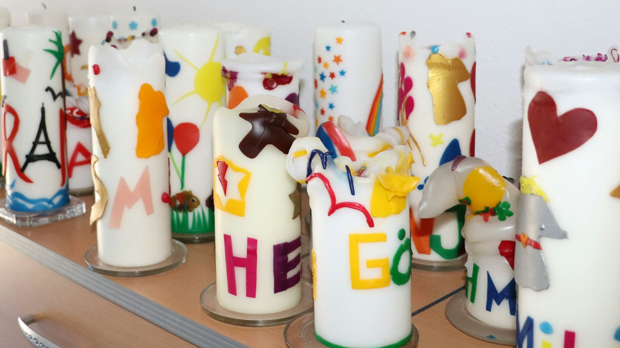 Viele bunte Kerzen mit Kindernamen stehen auf einer Kommode. Sie stehen symbolisch für je ein Kind, das von den ehrenamtlichen Mitarbeitenden des ambulanten Kinder- und Jugendhospizdienstes Köln vor seinem Tod begleitet wurde.