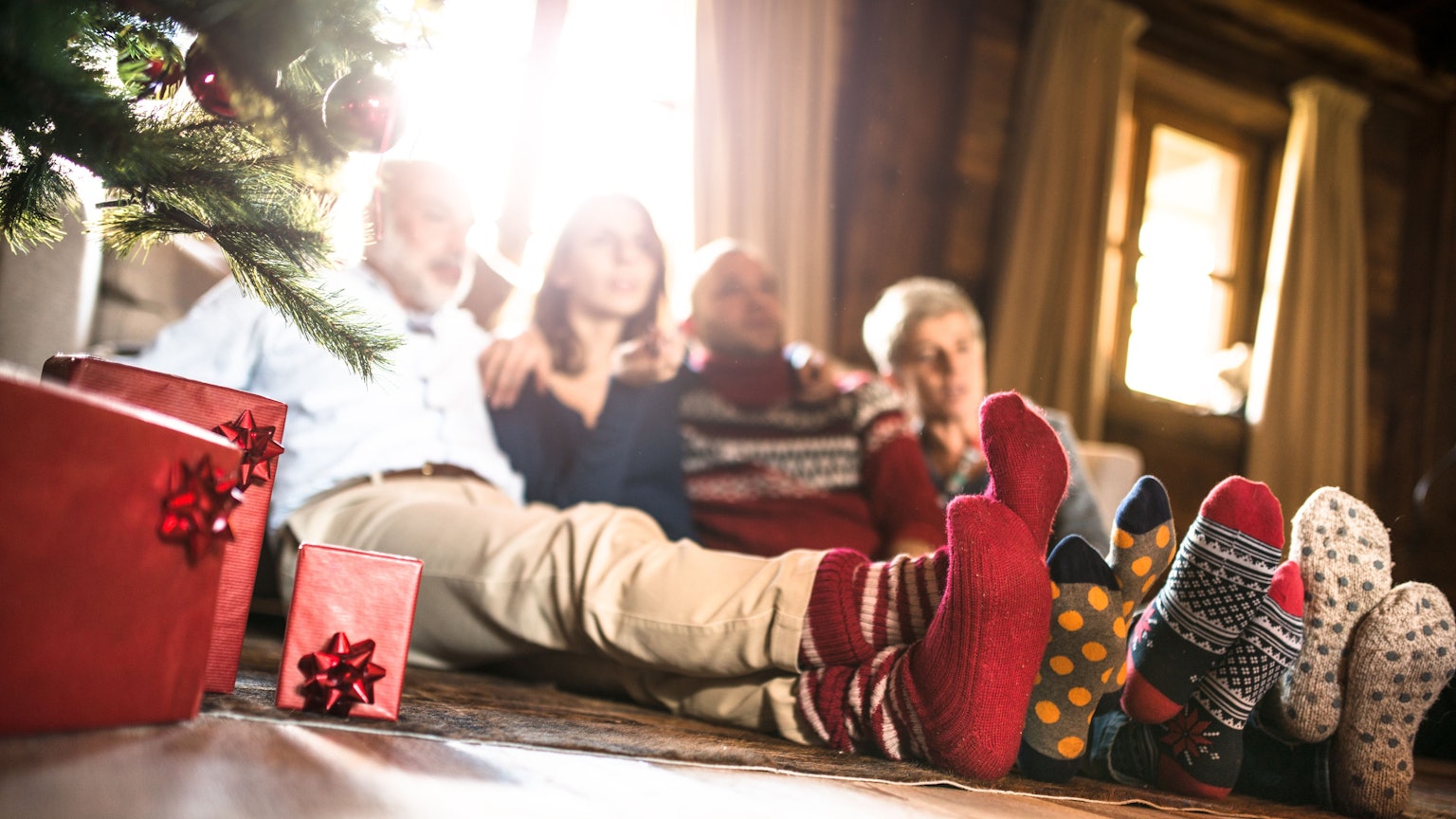 Eine Familie sitzt mit Wintersocken neben dem Weihnachtsbaum.