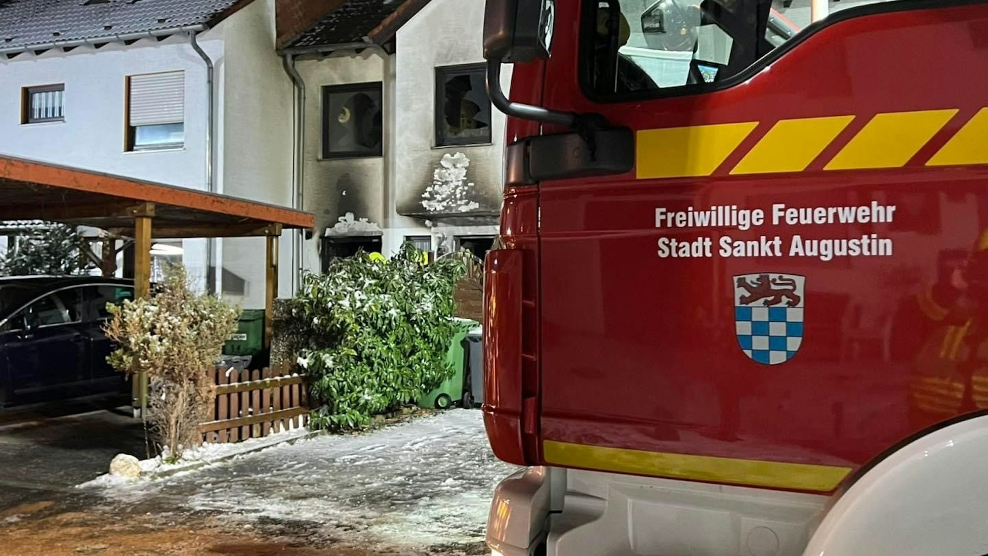 Ein Feuerwehrauto steht vor einem Haus, das von außen mit Russ verschmutzt ist.