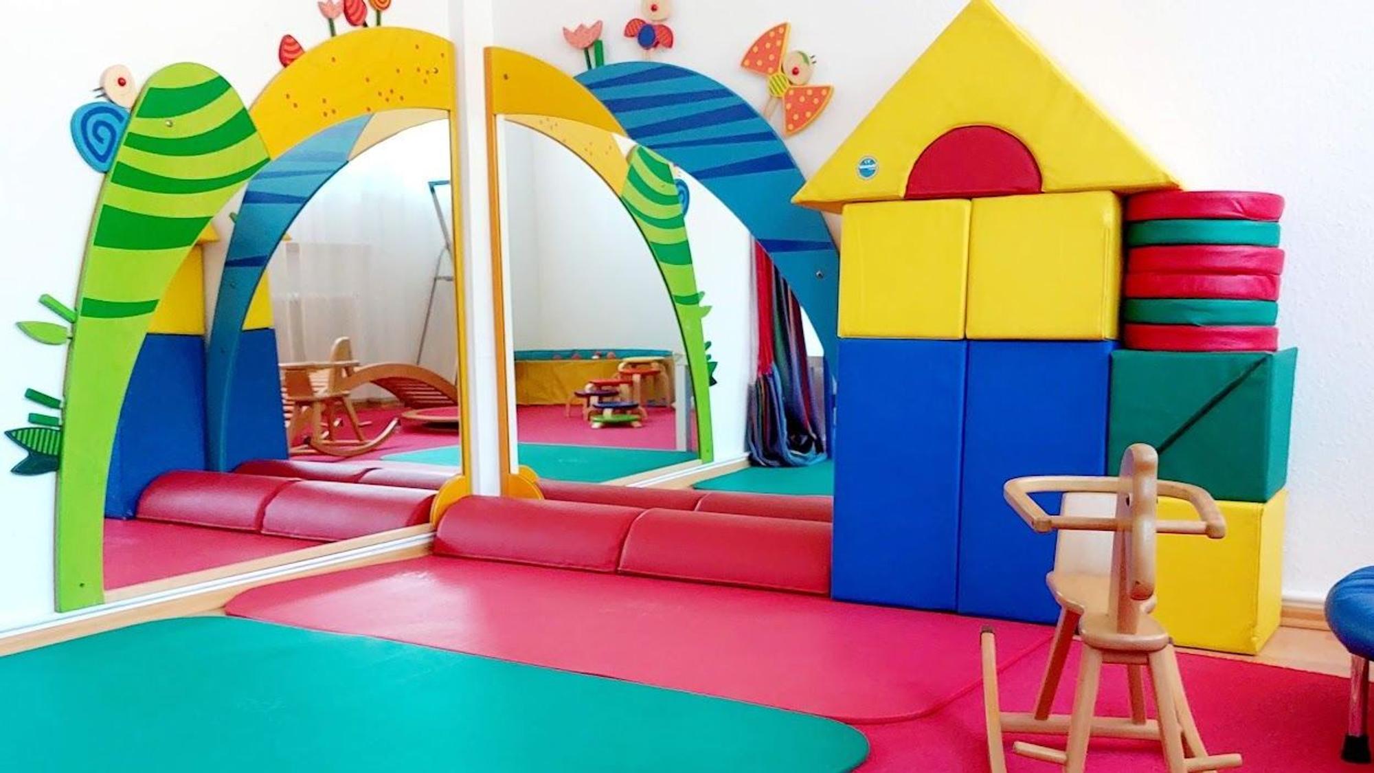 Ein Raum für Kinder mit bunten Matten und überdimensonal großen Bauklötzen, einem Schaukelpferd und großen Spiegeln.