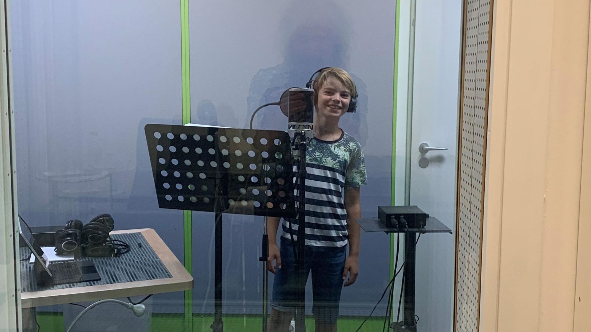 Theo von der Domsingschule steht mit Kopfhörern vor einem großen Mikrofon im Kölner Tonstudio.