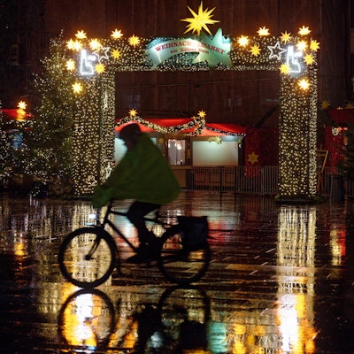 Ein Radfahrer fährt am frühen Morgen bei Schneeregen am Eingang des Weihnachtsmarkts am Dom vorbei.