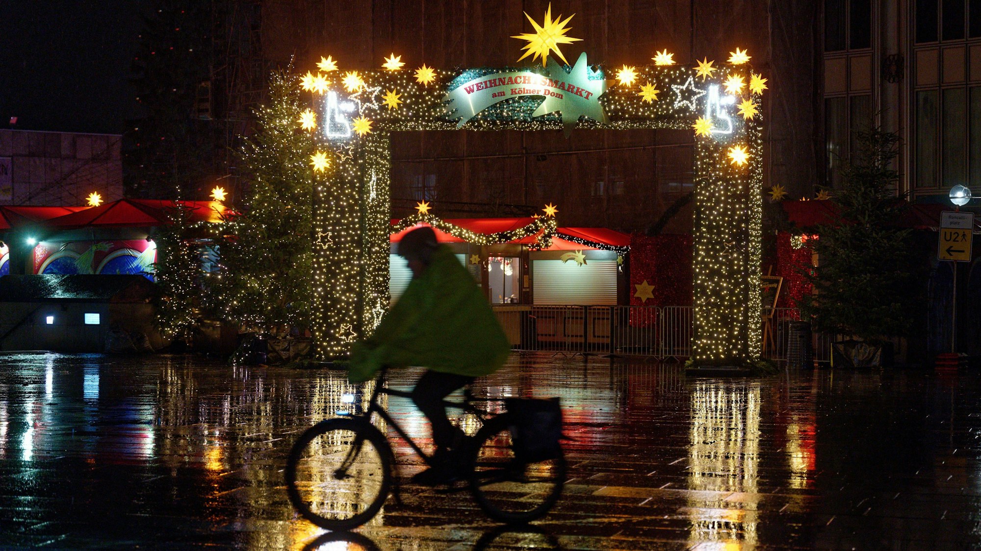 Ein Radfahrer fährt am frühen Morgen bei Schneeregen am Eingang des Weihnachtsmarkts am Dom vorbei.