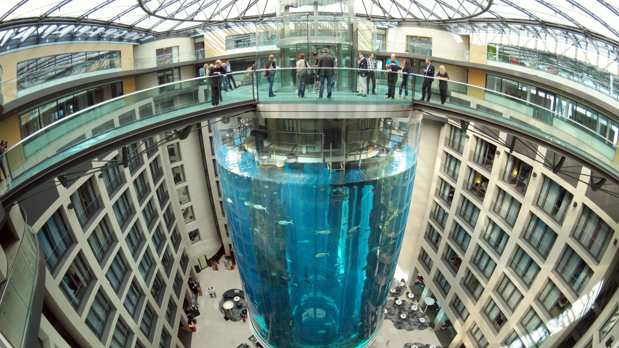 Blick auf den AquaDom als er noch nicht geplatzt war. Es ist ein großer Zylinder in der Mitte eines Hotels. Oben drüber ist eine Brücke, die zu dem Aufzug im Aquarium führen.