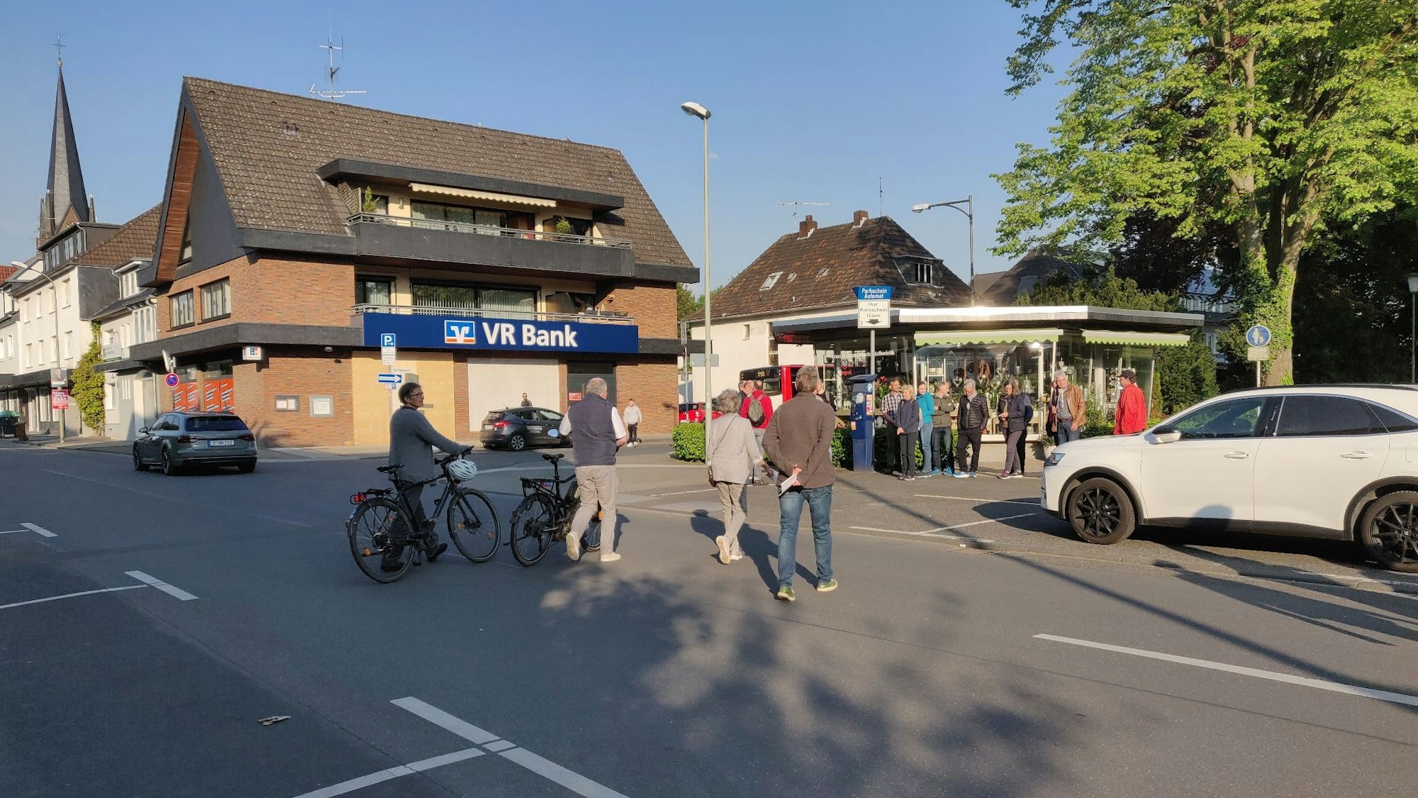 Fußgänger und Radfahrer überqueren die breite Kirchstraße zum Blumen-Pavillon am Stadtpark.