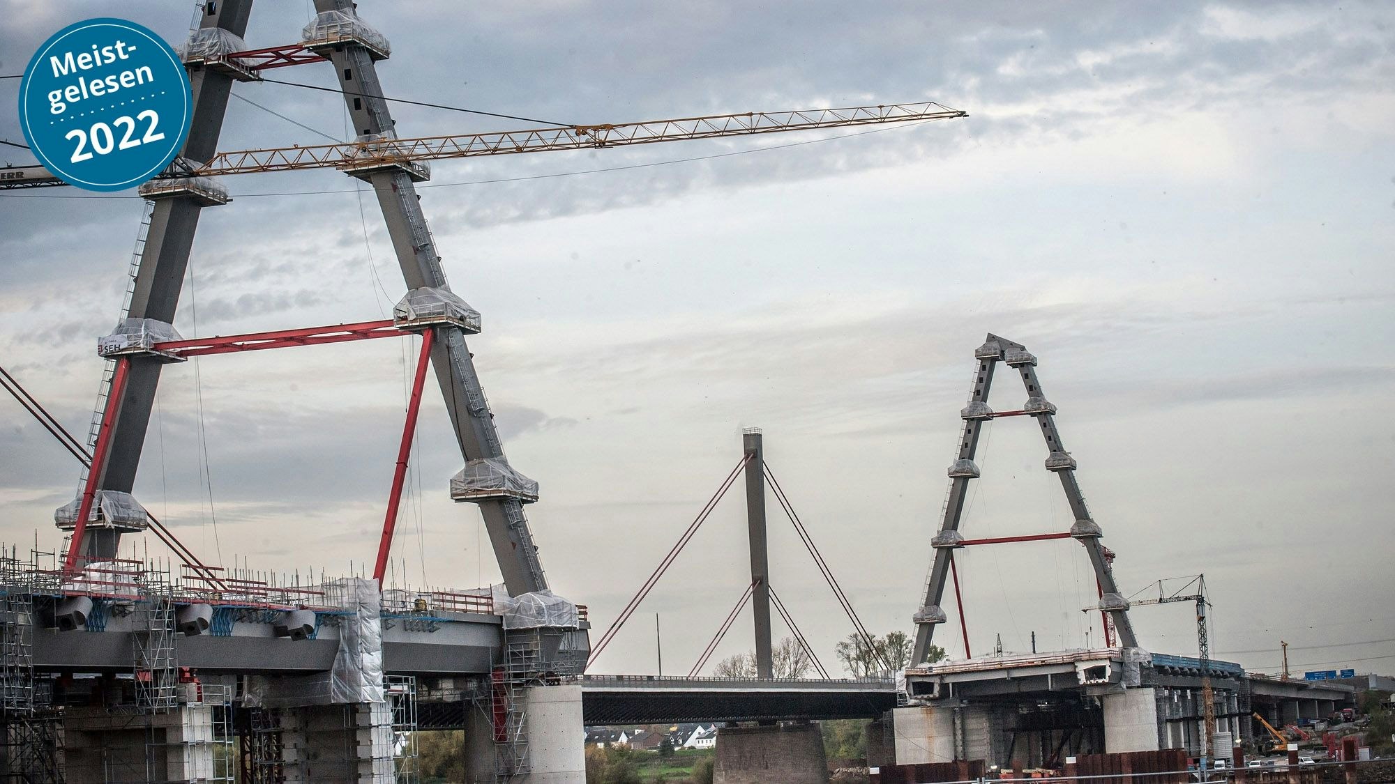 Die zwei neuen Pylone der Leverkusener Brücke sind im Vordergrund zu sehen. Es ist eine große Baustelle. Im Hintergrund ragt der alte Pylon in den leicht bedeckten Himmel.