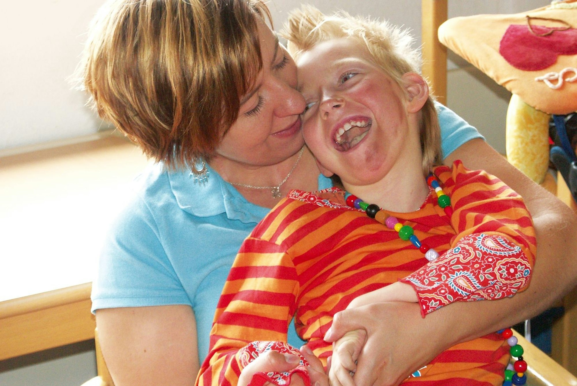 Eine Frau hält ein schwerkrankes Kind im Arm, es lacht aus vollem Herzen.