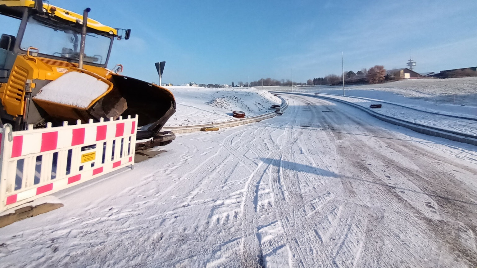 Noch führt die neue Straße bei Birk ins Nirgendwo. Sie soll die Neubauten an den Ort anbinden. Links ein Bagger hinter einer Straßenabsperrung. Mittig im Bild eine Straße im Schnee, die ins nichts führt.
