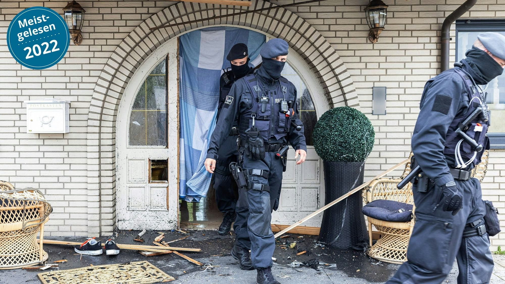 Polizisten verlassen in Leverkusen eine Villa durch eine zerstörte Eingangstür nach Durchsuchungen im Bereich der Clankriminalität.