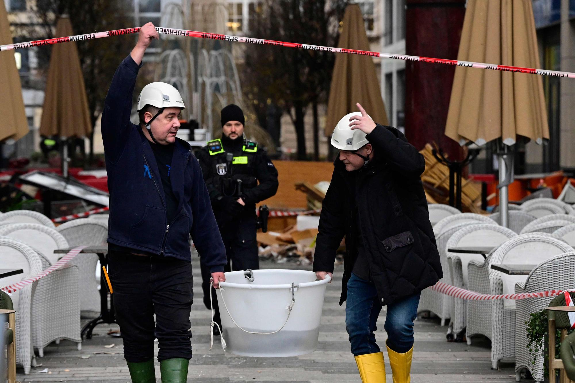 Rettungskräfte evakuieren lebende Fische in einem Eimer und gehen unter einer Absperrung her.