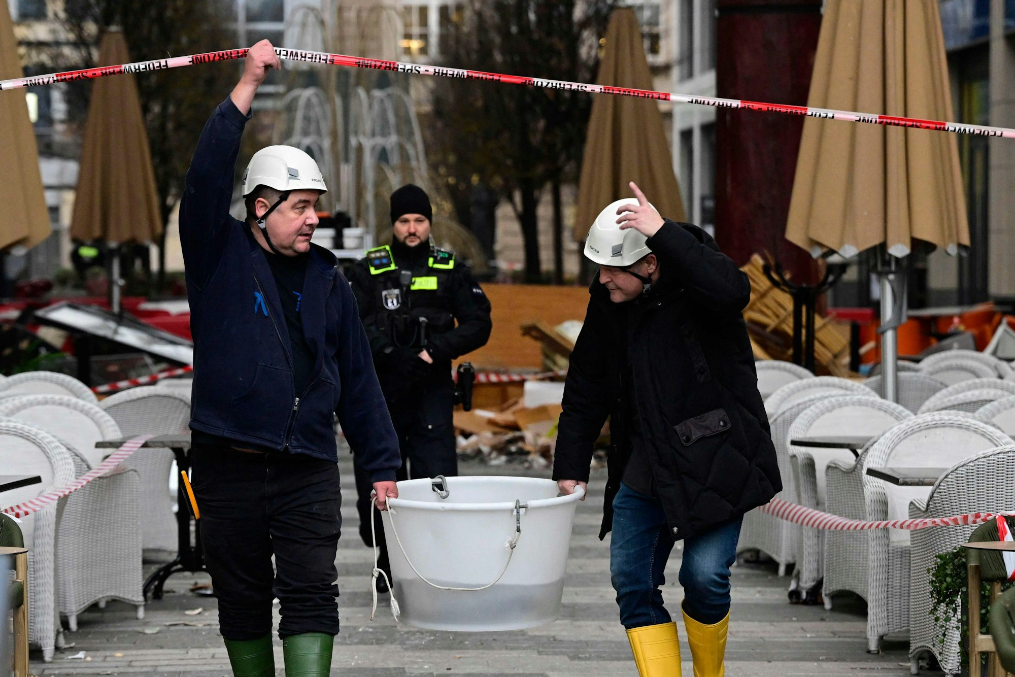 Rettungskräfte evakuieren lebende Fische in einem Eimer und gehen unter einer Absperrung her.