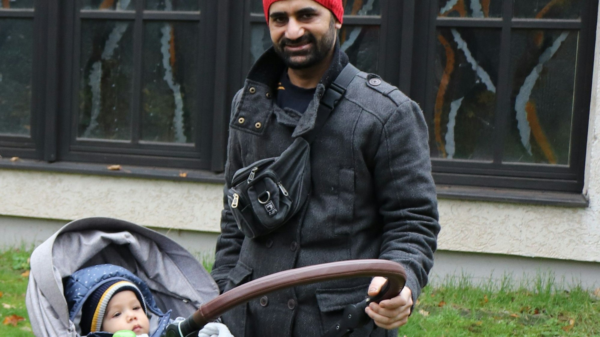 Ein junger Vater steht mit seinem Baby im Kinderwagen vor der St. Thomaskirche in Meschenich.