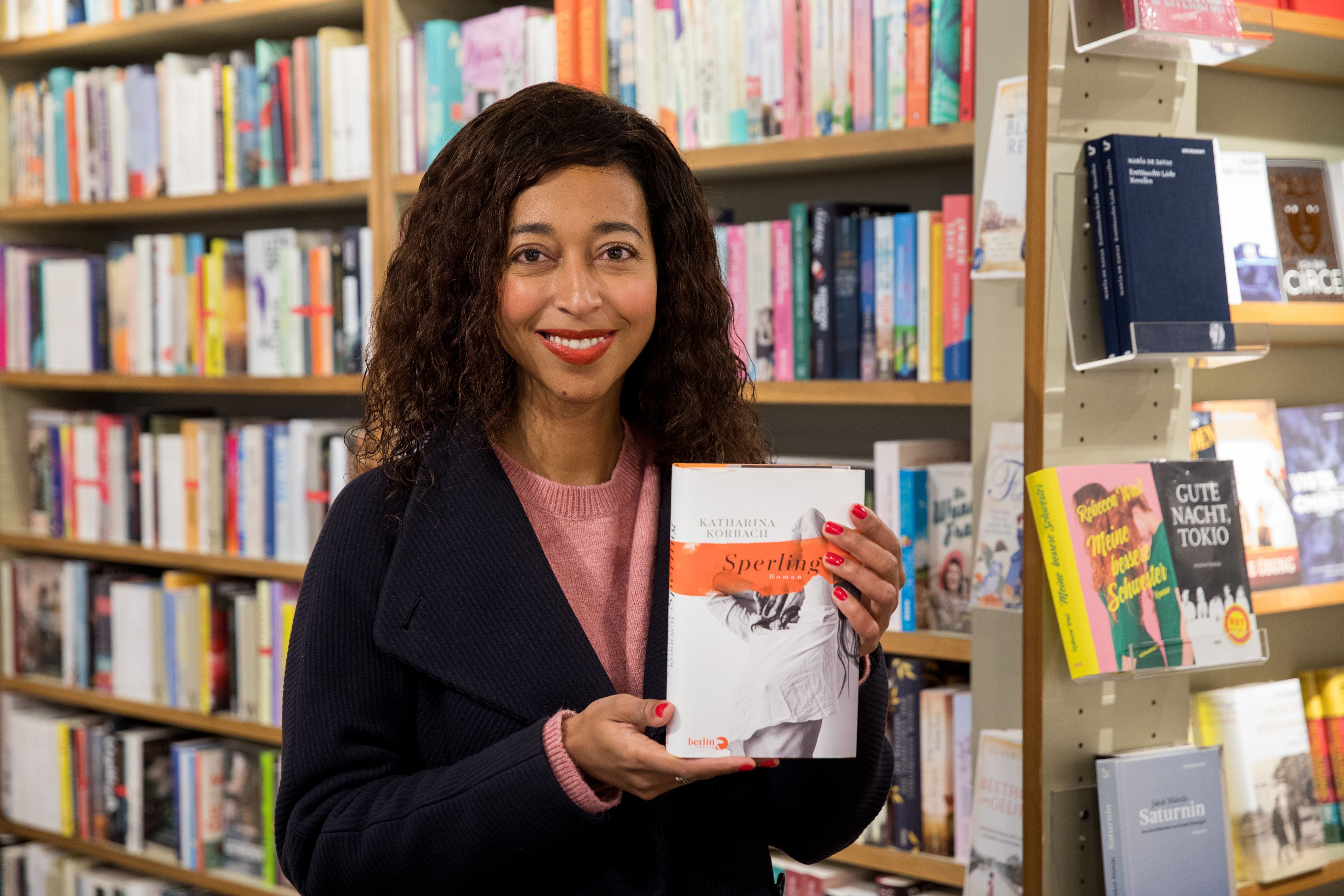 Die Autorin und Schriftstellerin Melanie Raabe steht mit dem Roman "Sperling" in der Hand vor einem Bücherregal.