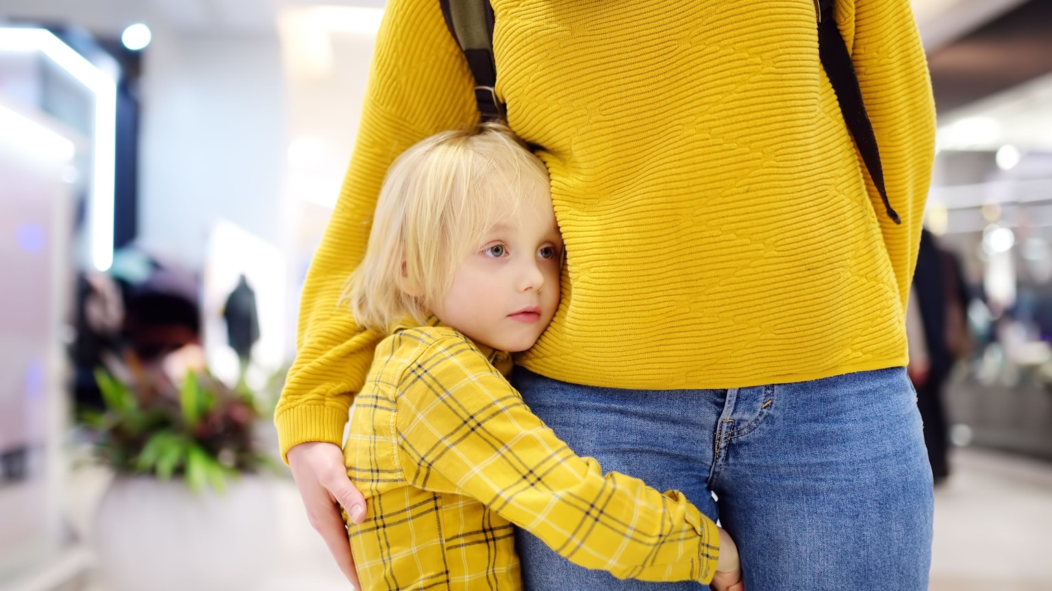 Ein kleiner Junge hält sich am Bein seiner Mutter fest.