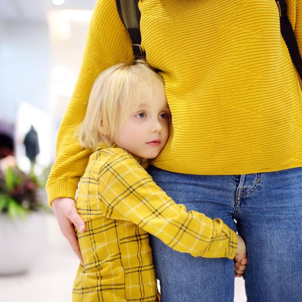 Ein kleiner Junge hält sich am Bein seiner Mutter fest.