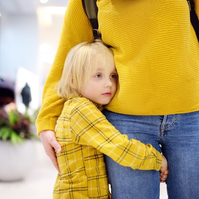 Ein kleiner Junge hält sich am Bein seiner Mutter fest.