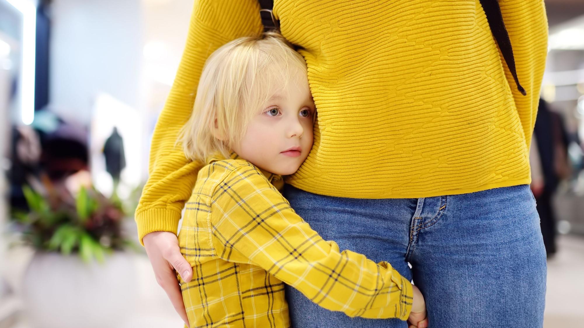 Ein kleiner Junge hält sich am Bein seiner Mutter fest.