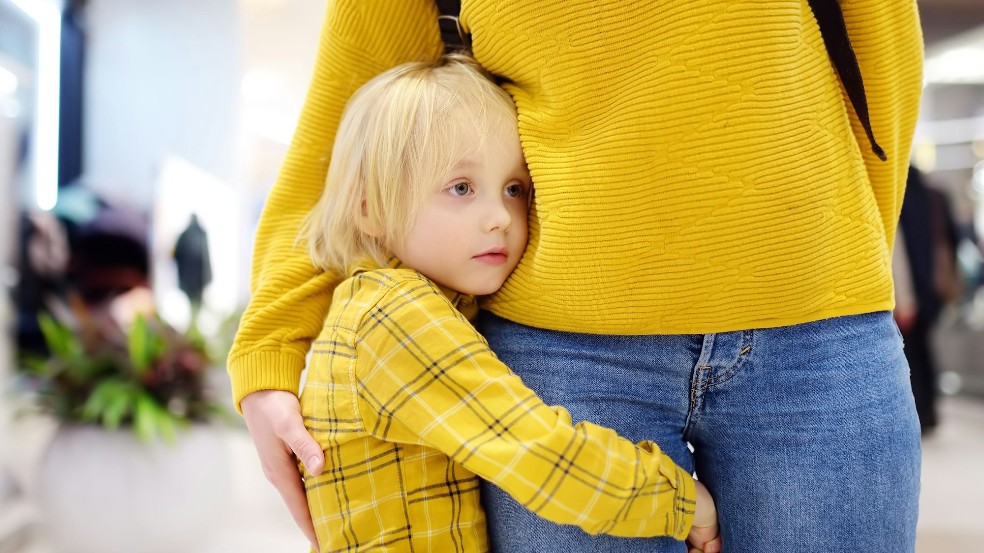 Ein kleiner Junge hält sich am Bein seiner Mutter fest.