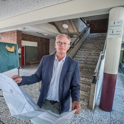 Wolfgang Kalski steht mit Bauplänen in der Hand im Foyer der Grundschule Büscherhof
