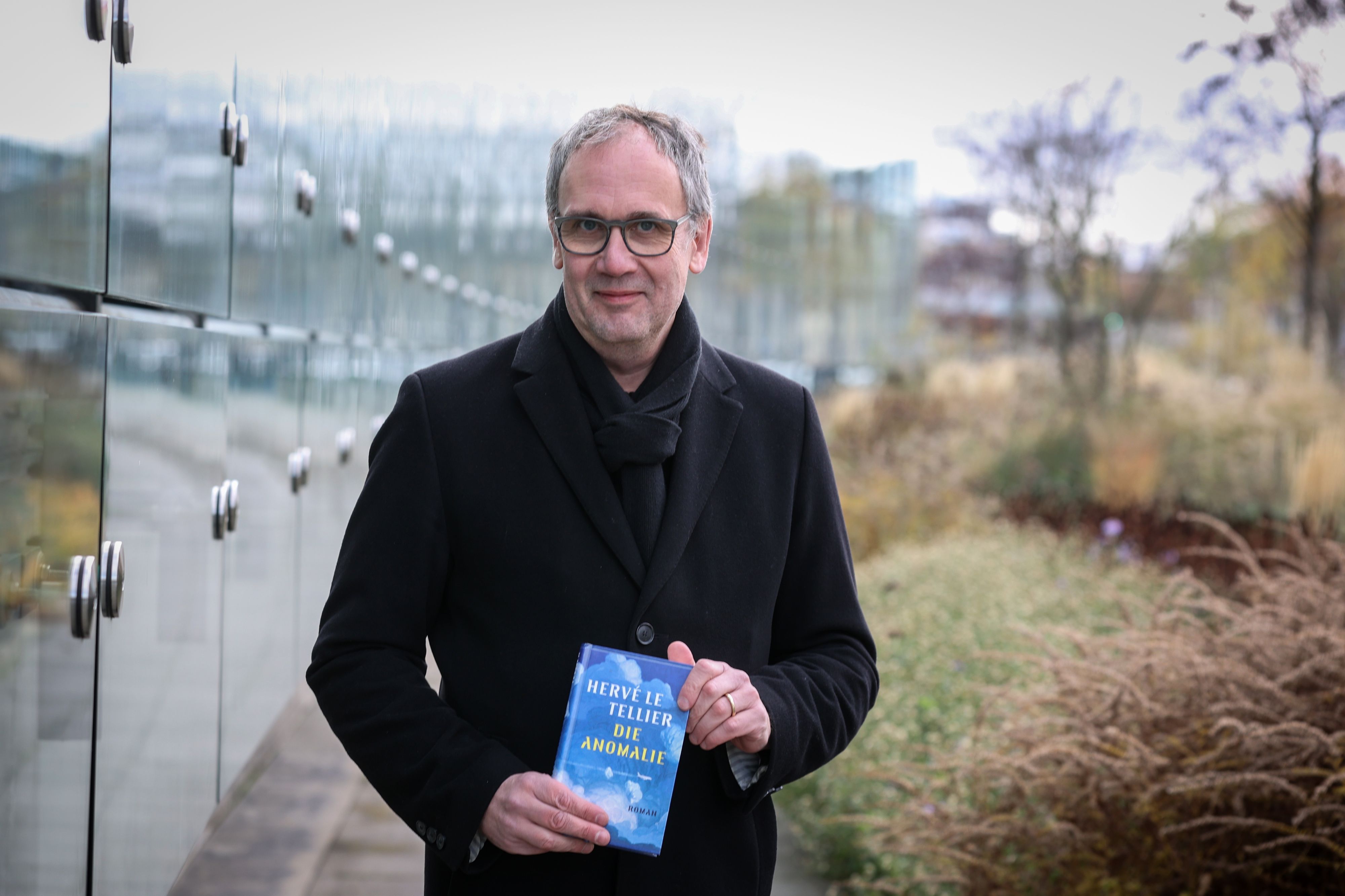 Bestseller-Autor Volker Kutscher steht in einem schwarzen Mantel vor dem Neven DuMont Haus