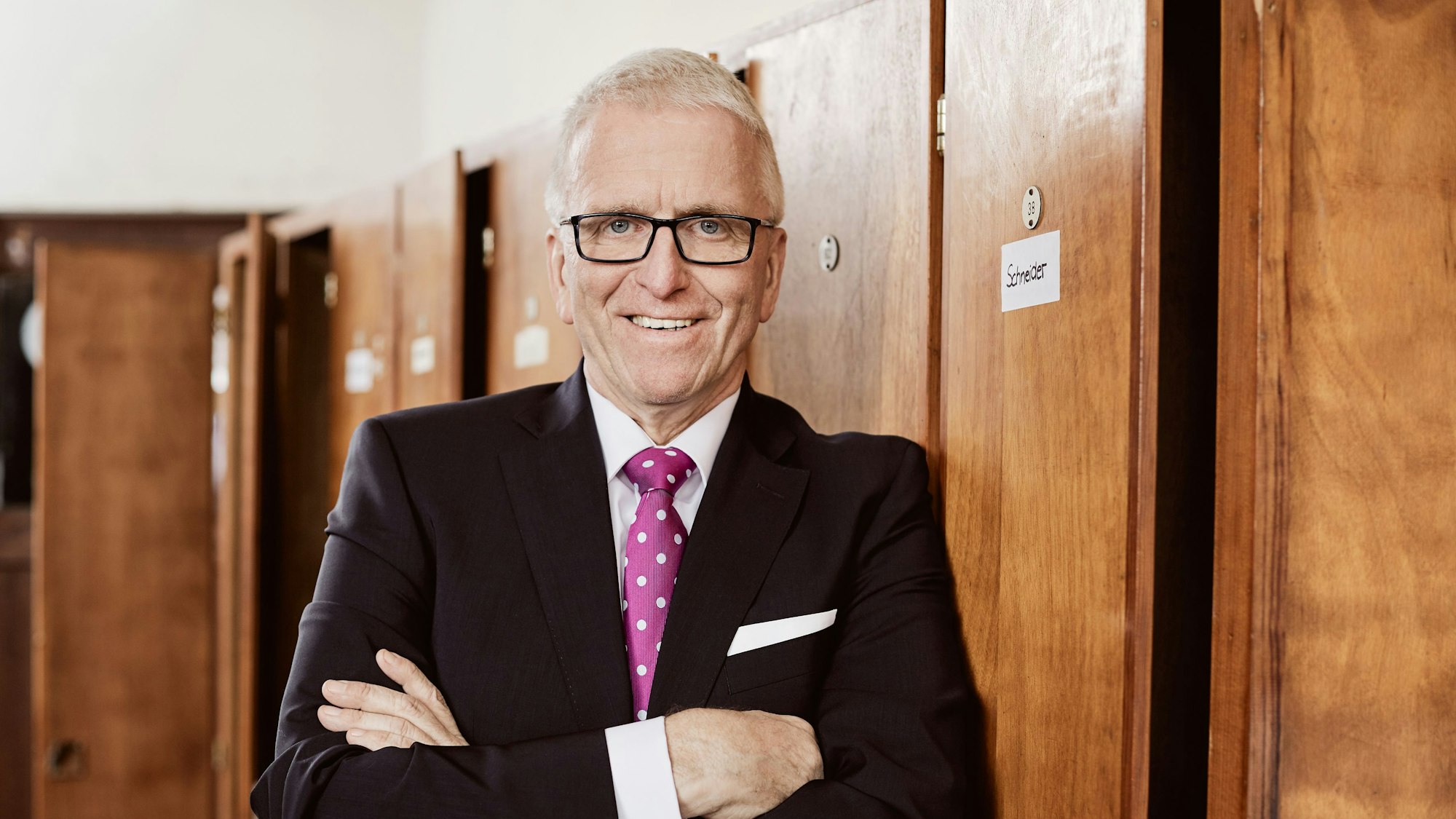 Manfred Schneider, Volksbank Oberberg vor einem Holzschrank im Anzug