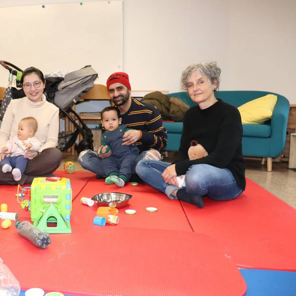 Drei Eltern sitzen mit ihren Babys und einer Diplom-Heilpädagogin auf knallroten Matten, vor ihnen liegt allerhand Spielzeug.