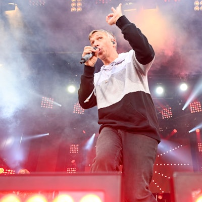 Kasalla-Sänger Bastian Campmann singend auf der Bühne im Gegenlicht von Scheinwerfern und umgeben von Nebel.