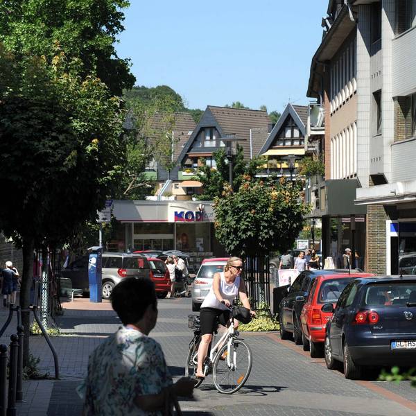 Blick in die Brückenstraße Richtung Kodi mit geparkten Autos, Fußgängern und einer Radfahrerin.