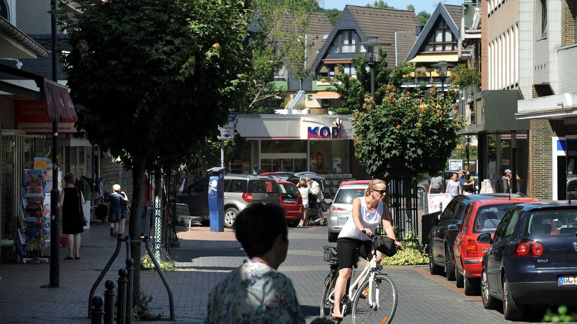 Blick in die Brückenstraße Richtung Kodi mit geparkten Autos, Fußgängern und einer Radfahrerin.