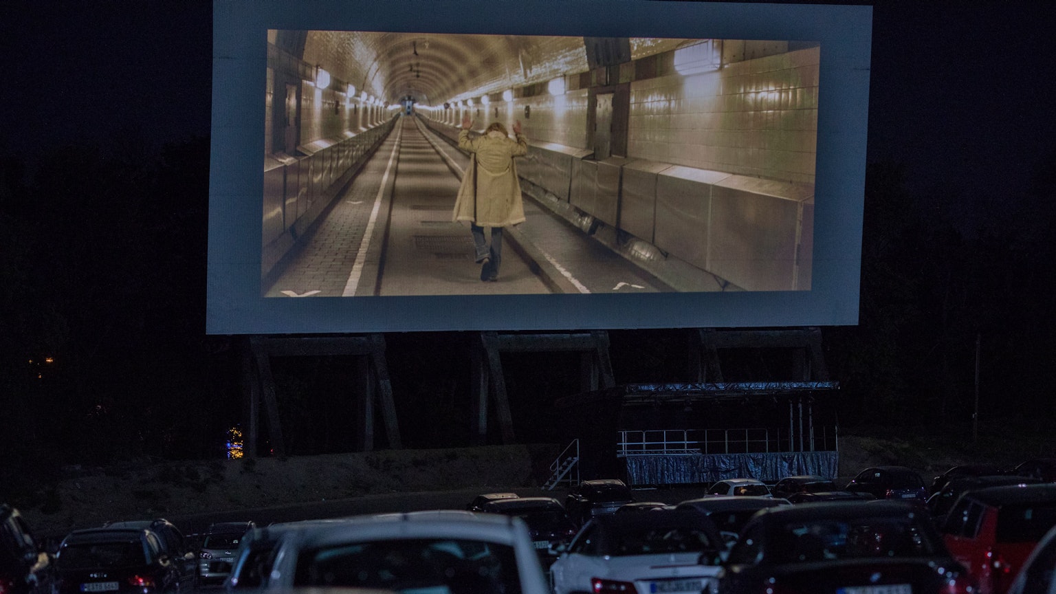 Viele Autos stehen vor einer großen Leinwand im Autokino in Köln-Porz. Auf der Leinwand läuft ein Film.
