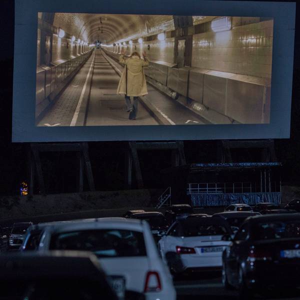 Viele Autos stehen vor einer großen Leinwand im Autokino in Köln-Porz. Auf der Leinwand läuft ein Film.