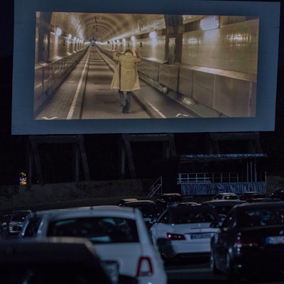 Viele Autos stehen vor einer großen Leinwand im Autokino in Köln-Porz. Auf der Leinwand läuft ein Film.