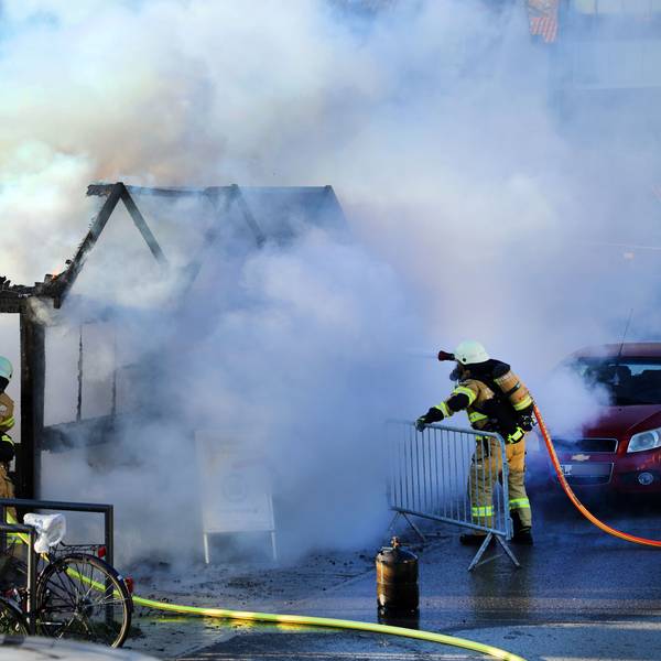 Zwei Feuerwehrleute löschen ein brennendes Holzhäuschen. Große Rauchwolken steigen auf.
