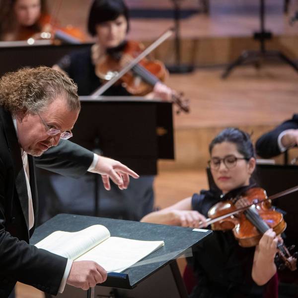 Der französische Dirigent Stéphane Denève beugt sich über sein Pult, im Hintergrund sind Musiker zu sehen.