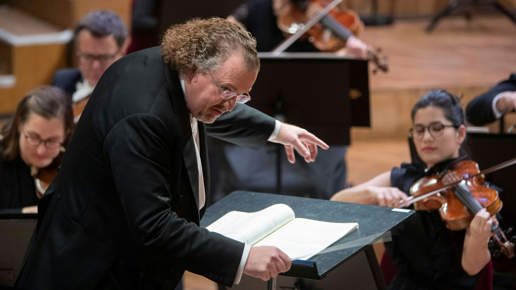 Der französische Dirigent Stéphane Denève beugt sich über sein Pult, im Hintergrund sind Musiker zu sehen.