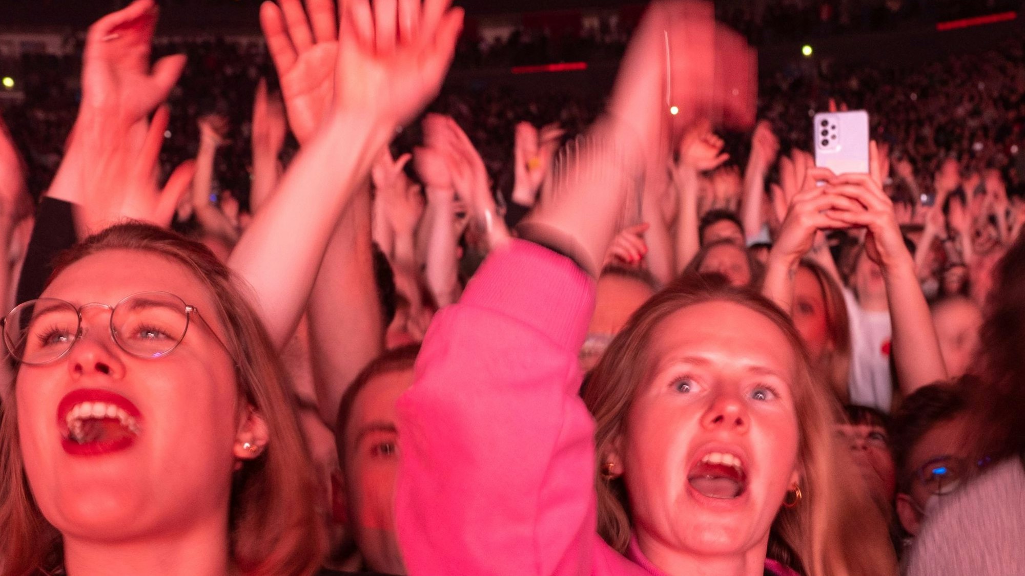 Das Publikum hat die Arme nach oben ausgestreckt, die Münder sind beim Kreischen oder Singen weit geöffnet.