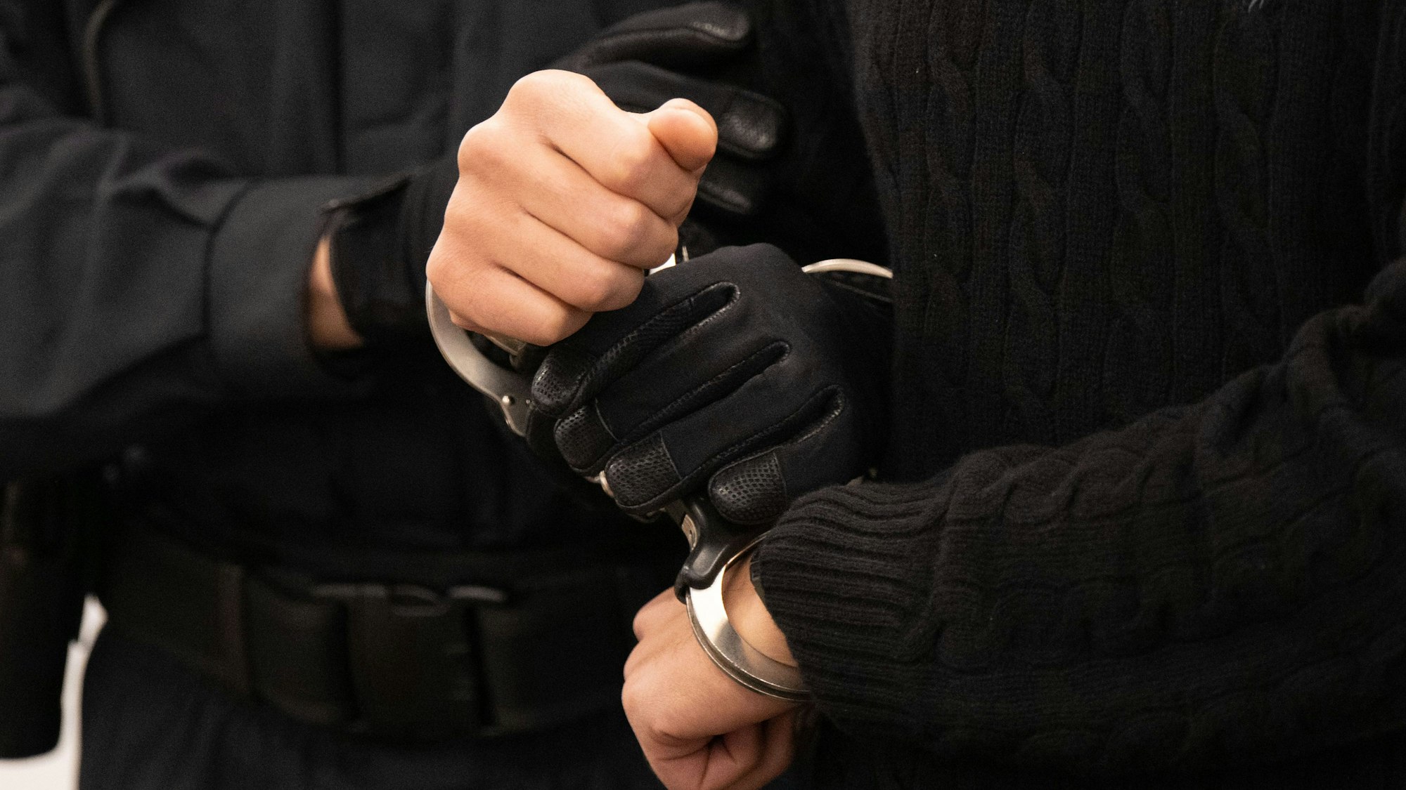 Ein Polizist hält Hände von Gefangenen in Handschellen