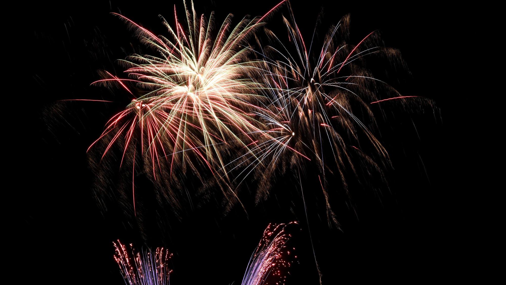Silvesterraketen hinterlassen sternförmigen Funkenregen an einem Nachthimmel.