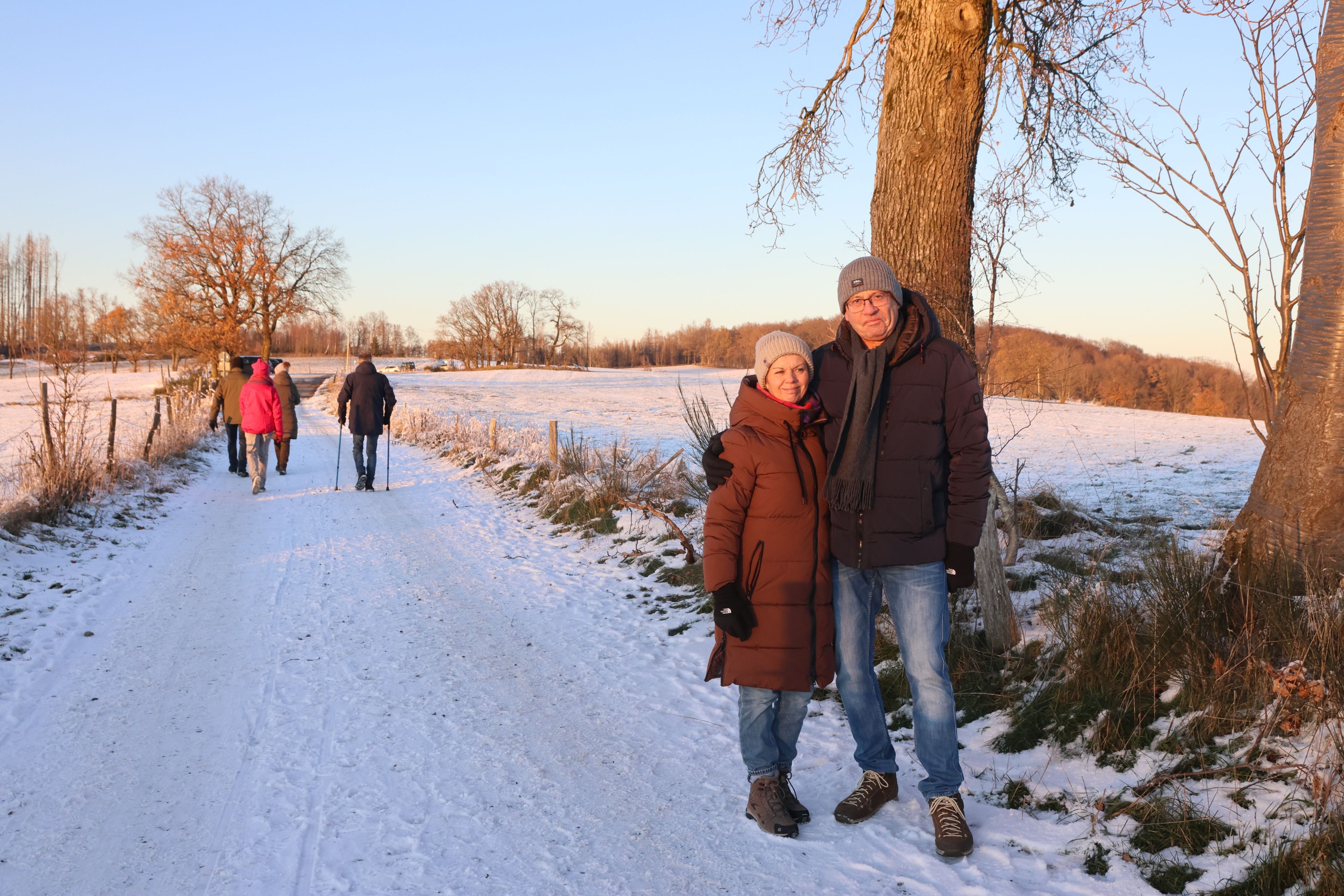 Ilona und Karl-Heinz Schenk stehen Arm in Arm auf einem verschneiten Wanderweg. Im Hintergrund taucht die Sonne die Landschaft in rötliches Licht