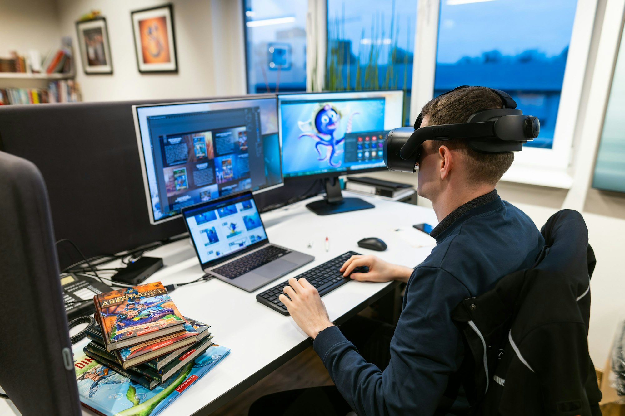 Ein Mann sitzt mit VR-Brille an einem Arbeitsplatz mit mehreren PC-Bildschirmen.