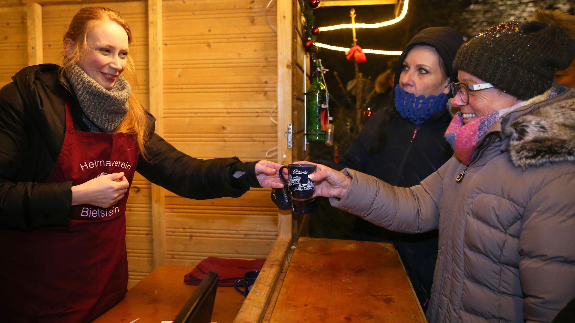 Unsere Autorin Lilian Kraft (l.) reicht eine Tasse Glühwein über den Tresen. Sie half am Samstag auf dem Bielsteiner Weihnachtsmarkt in der Glühweinbude des Heimatvereins mit und berichtet hier.