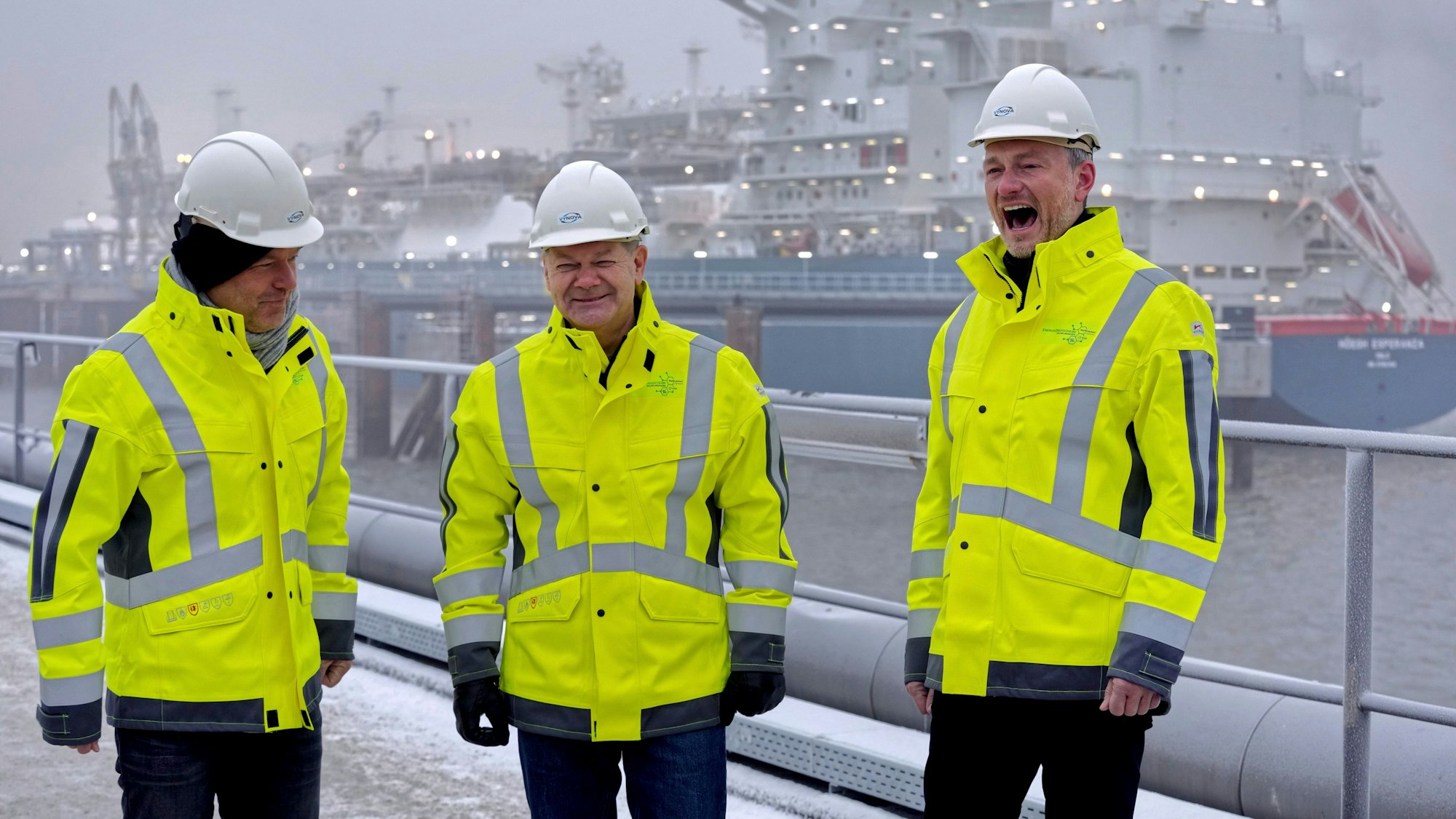 Ribert Habec, Olaf Scholz und Christian Lindner stehen bei der Eröffnung des ersten deutschen LNG-Terminals in Wilhelmshaven vor dem Spezialschiff „Höegh Esperanza“.