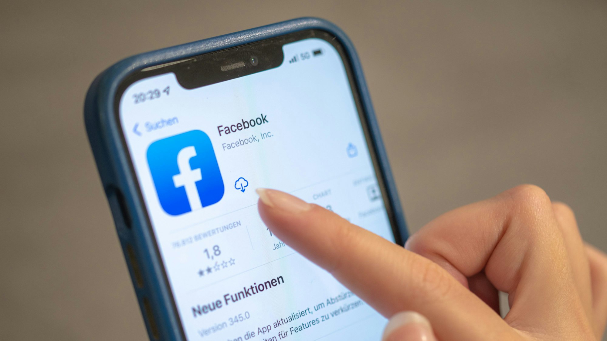 Das Facebook-Logo ist auf einem Handy zu sehen. Eine Frauenhand tippt auf das Download-Icon neben dem Logo.