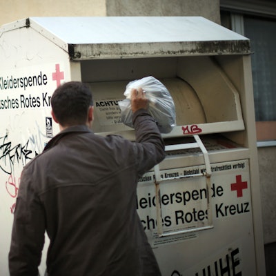 Ein Mann wirft Kleidung in einen Altkleider-Container.