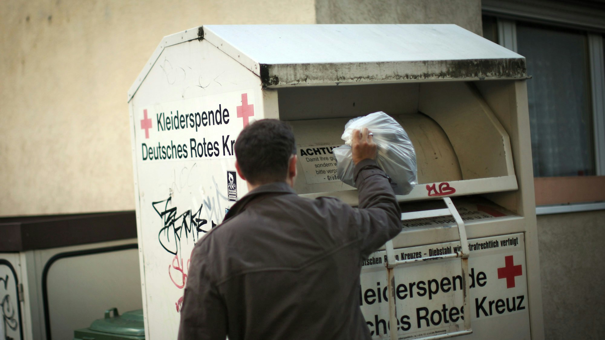 Ein Mann wirft Kleidung in einen Altkleider-Container.