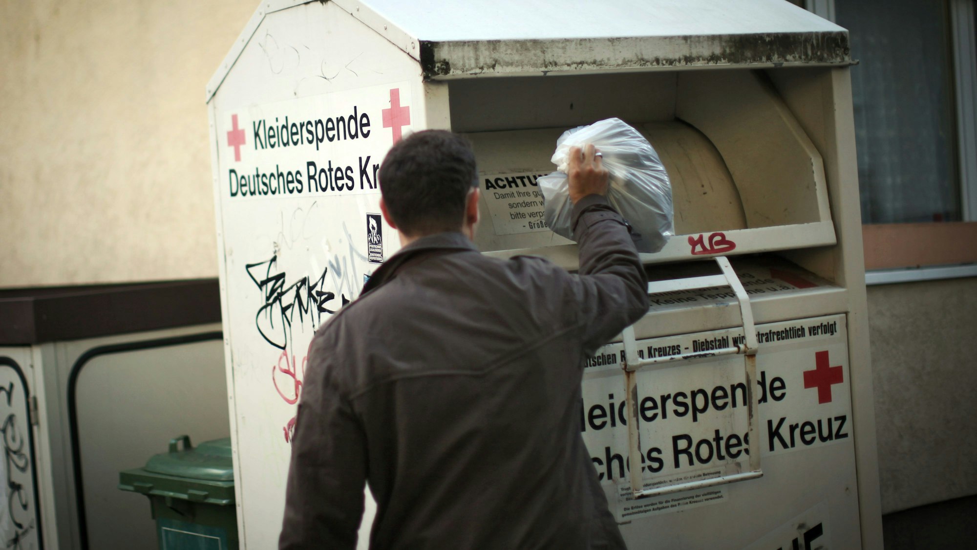 Ein Mann wirft Altkleider in einen Sammelcontainer.