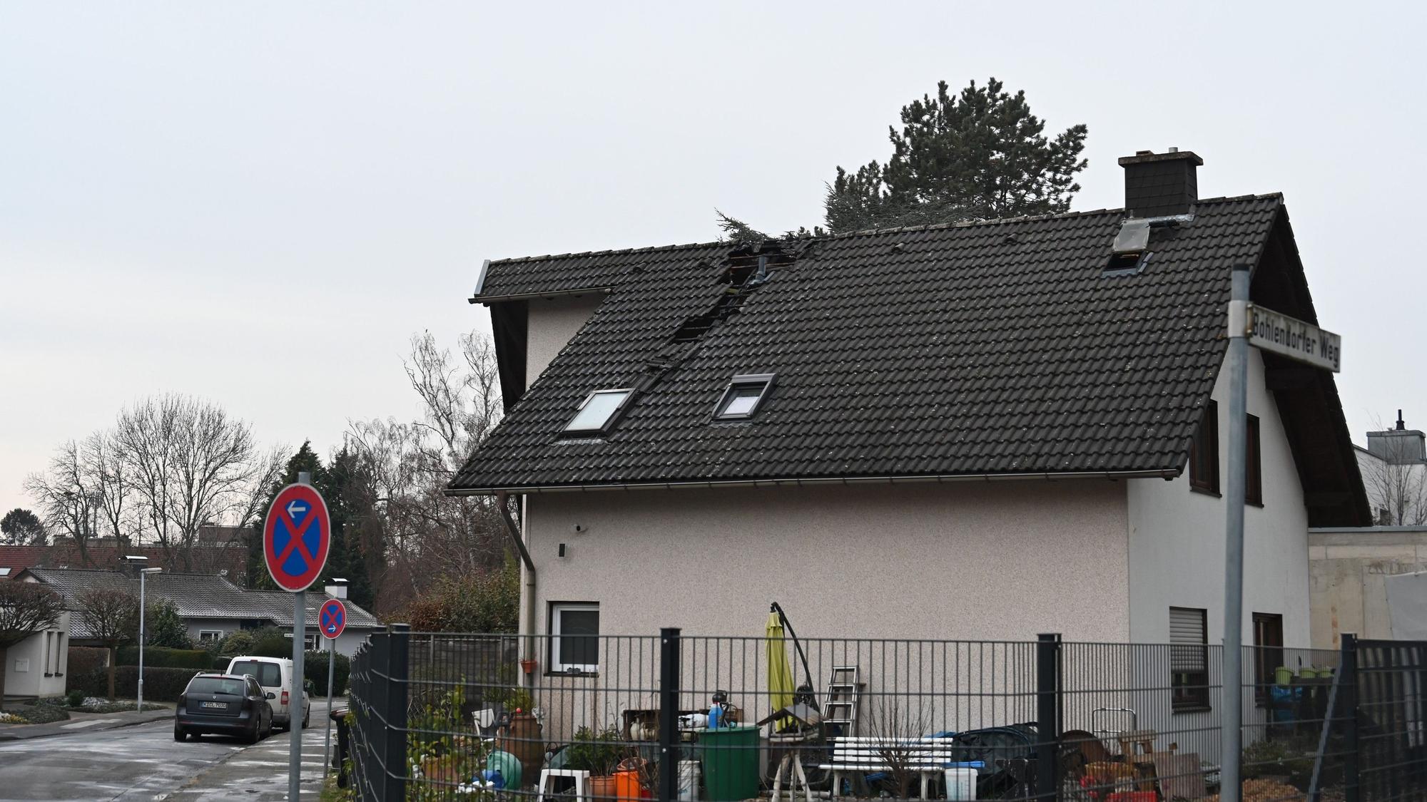 Man sieht ein Haus, in dessen Dach Pfannen fehlen. Der Riss zieht sich vom Dachfirst bis zur Hälfte der Dachlänge.