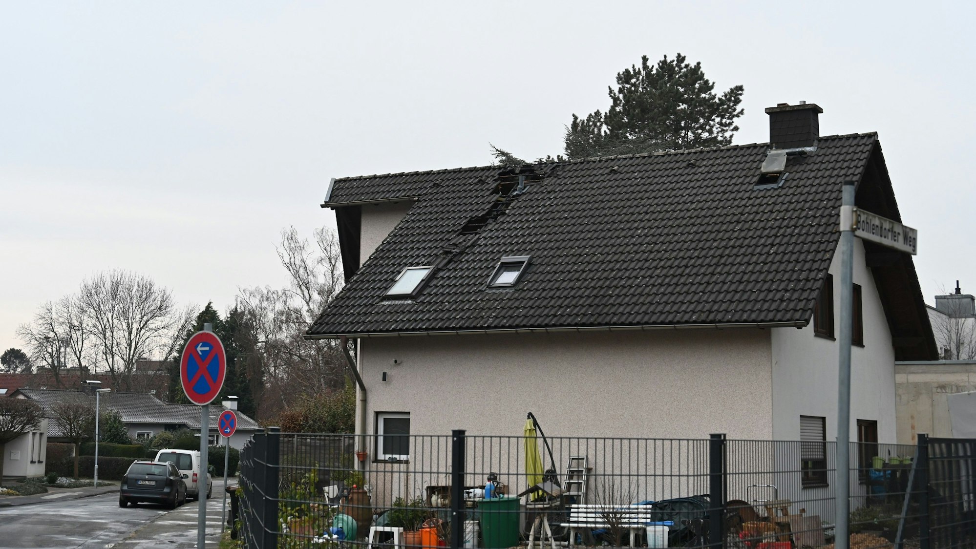 Man sieht ein Haus, in dessen Dach Pfannen fehlen. Der Riss zieht sich vom Dachfirst bis zur Hälfte der Dachlänge.