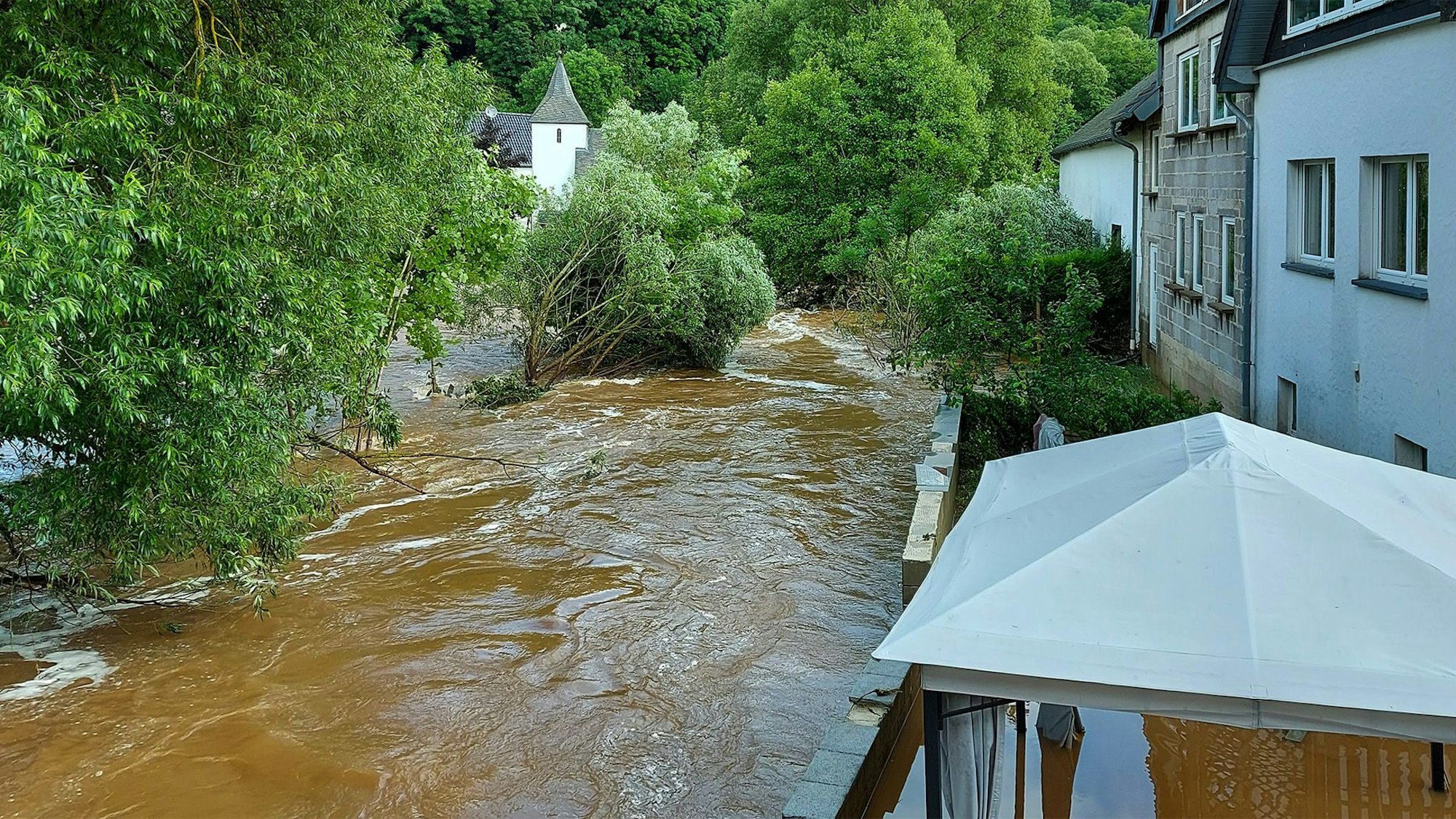 Blick auf Kronenburgerhütte mit der Brigida-Kapelle im Hintergrund in Dahlem. Inmitten der Fluss Kyll, der sich zu einem reißenden Strom entwickelte.