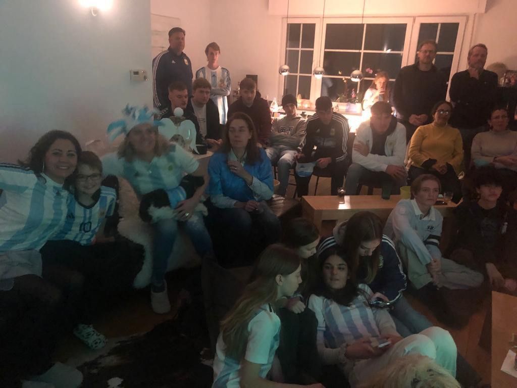 Mehr als 20 Leute sitzen in Trikots und mit Fahnen vor dem Fernseher.